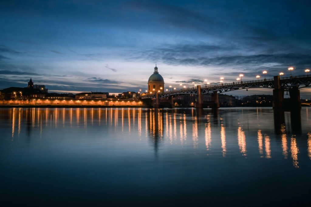Serene twilight view of Pont Saint-Pierre and Garonne River in Toulouse, France, with city lights reflecting in the water.